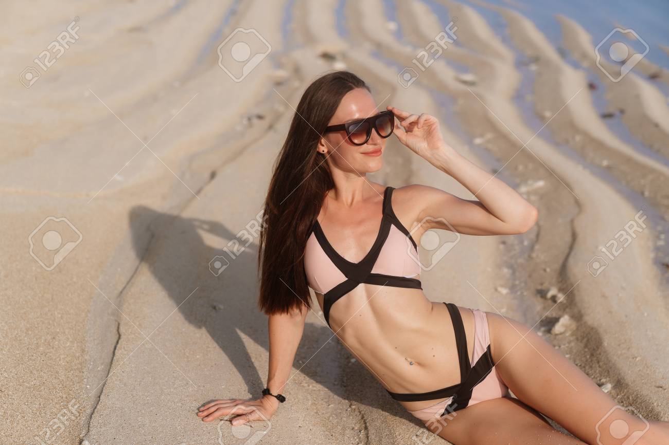 Sexy girl in swimsuit and sunglasses lies on white sandy beach near ocean - 116767119