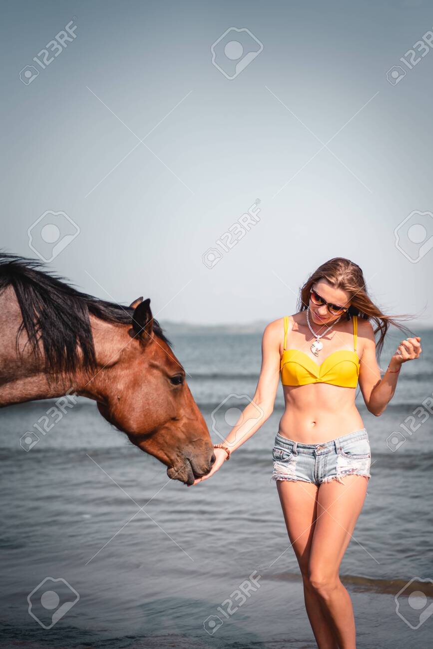 Portrait of smiling woman and a horse on the beach - 131536101