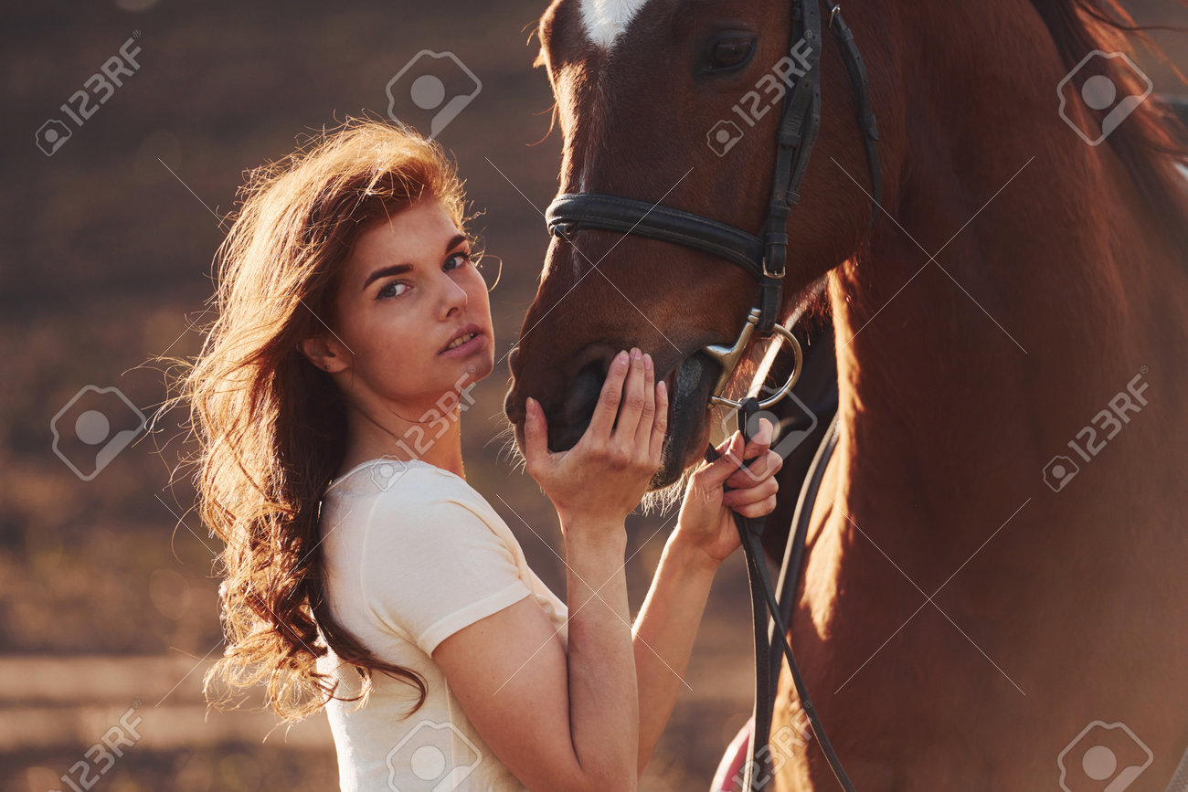 Young woman standing with her horse in agriculture field at sunny daytime - 201594235