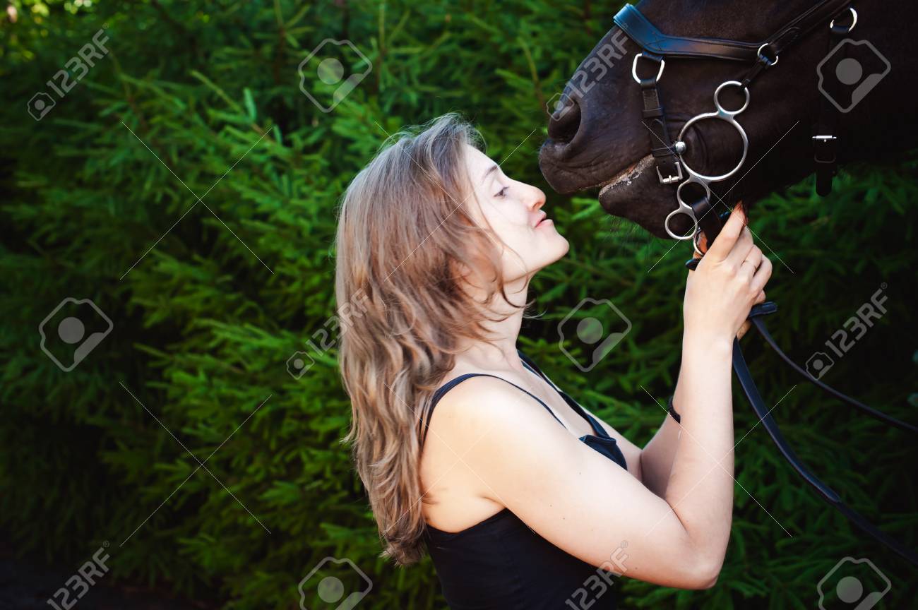 Emotional  Portrait of a female in love with horses, black Friesian stallion thoroughbred pet, outdoors. - 83786226