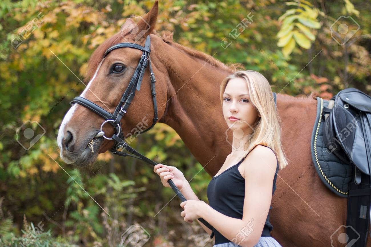 a young, blonde girl posing with a horse, a beautiful girl and a strong horse. in the forest - 91536931